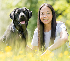 A woman sitting in the grass with a black Labrador