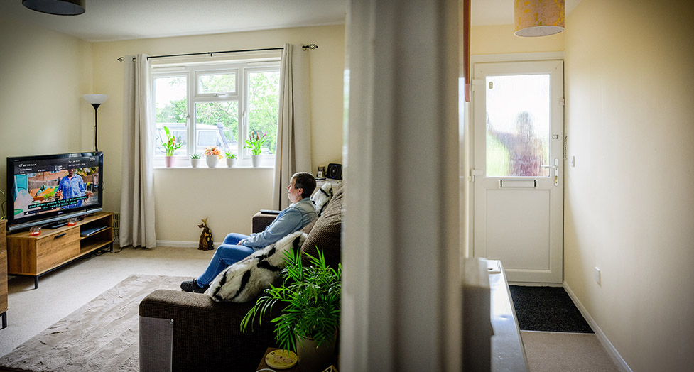 Jackie is sitting on a sofa watching TV while someone is at the door pressing the doorbell