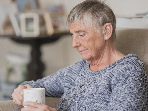 A woman holding a white cup looks saddened