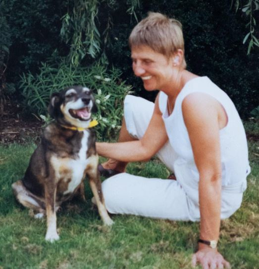a smiling woman sitting on grass next to a dog