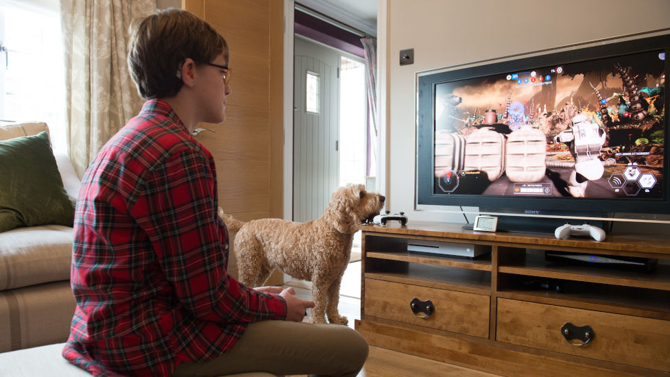 WIlliam playing on his xbox while hearing dog Nutmeg looks on