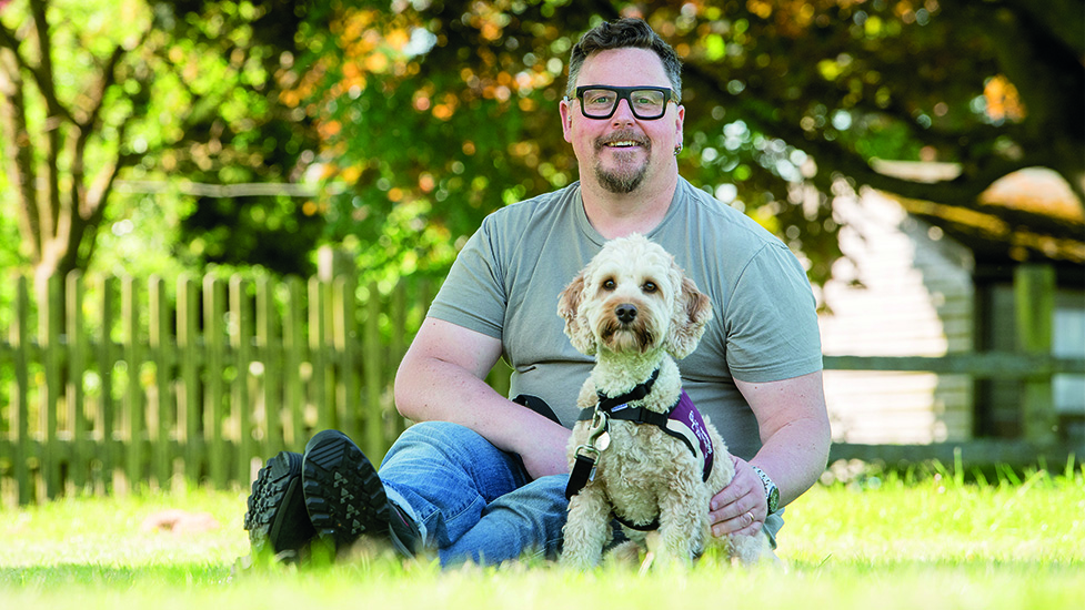 Lee and cockapoo Juno sitting together on the grass looking at the camera