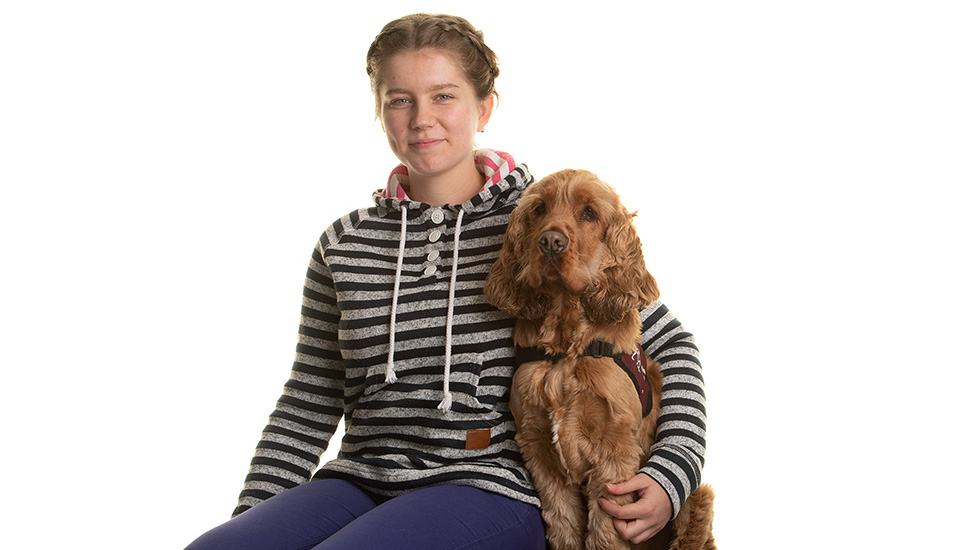 Trinity and cocker spaniel Alvin sitting next to each. Trinity's left arm is around Alvin