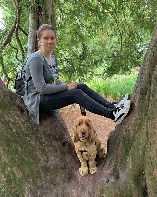 Trinity is sitting across two tree trunks while Alvin is underneath her legs standing up