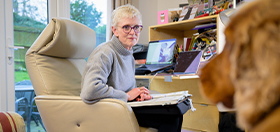 Ann is sitting on a chair in front of a laptop and she has turned round to face golden cocker spaniel Gryffin, who is to the right of the photo