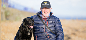 Deryck is sitting on the beach with his arm around hearing dog Elroy