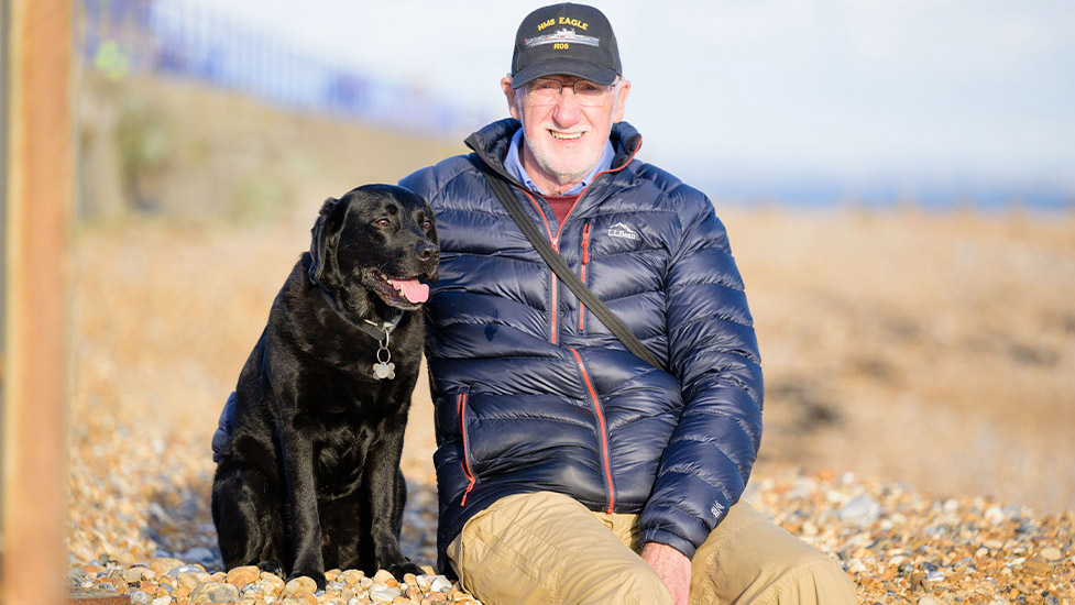 Deryck is sitting on the beach with his arm around hearing dog Elroy