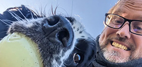 Hearing dog Harry with a ball in his mouth next to his deaf parter Neil